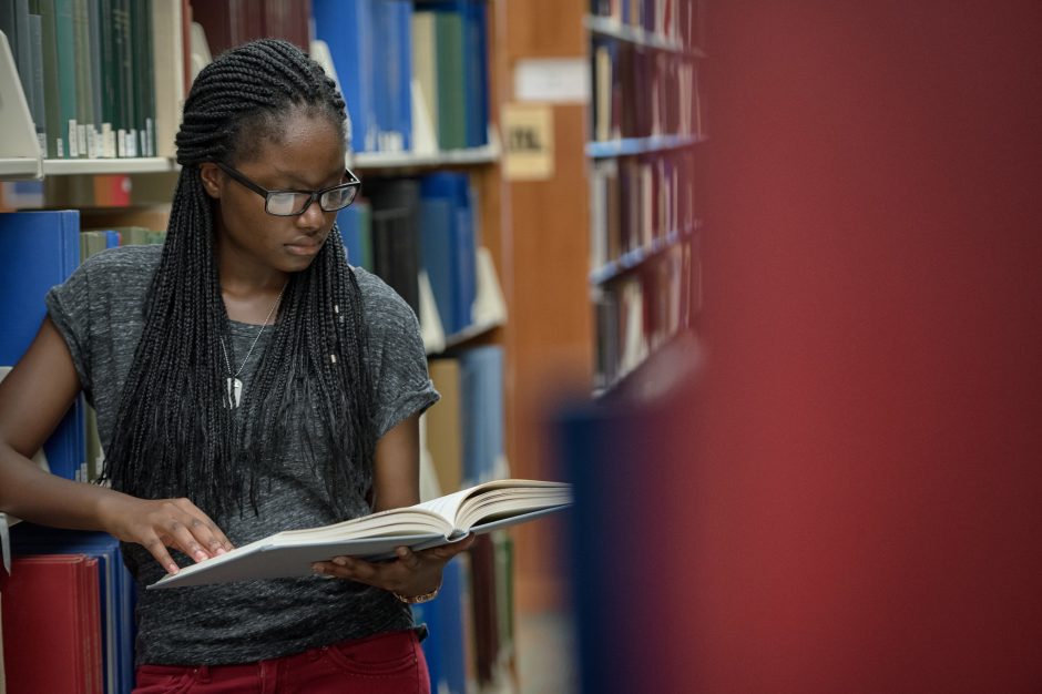 A student fully engaging in reading a book by a library stack.