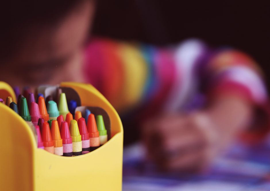 Child drawing with a pack of crayons in front of them
