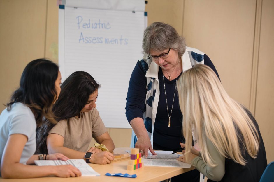 Three students learn about pediatric assessments from their professor