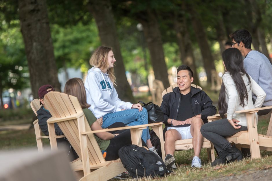 A group of students sitting in outdoor chairs chatting and laughing.