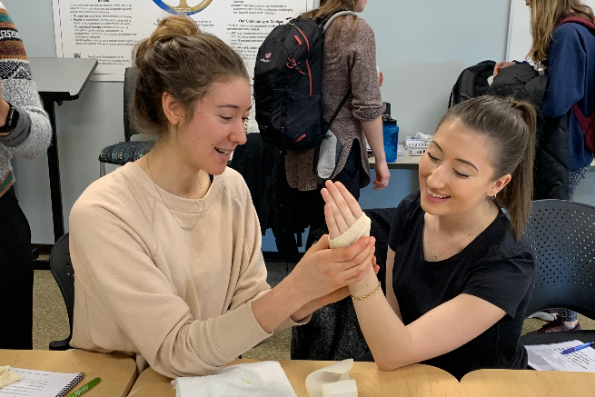 Two occupational therapy students learning how to apply hand supports.