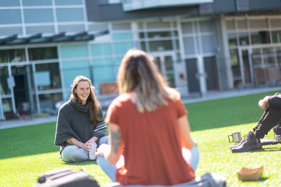 A group of students sitting on the grass in conversation.