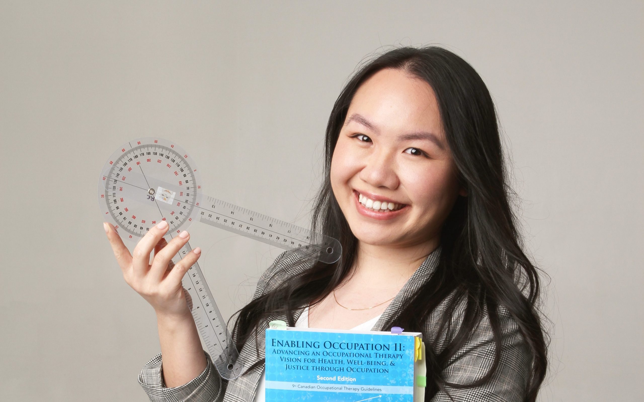 A professional headshot of Rosemary, who is holding a compass and a textbook about occupational therapy