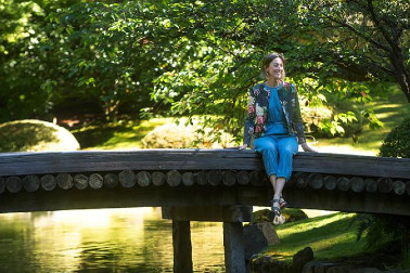 Katie Bunting sitting on a bridge in a sunlit Nitobe Garden