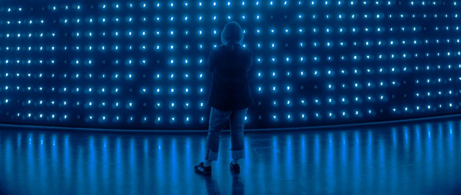 Person looking to the back of a stage which has hundreds of blue lights arranged in a grid